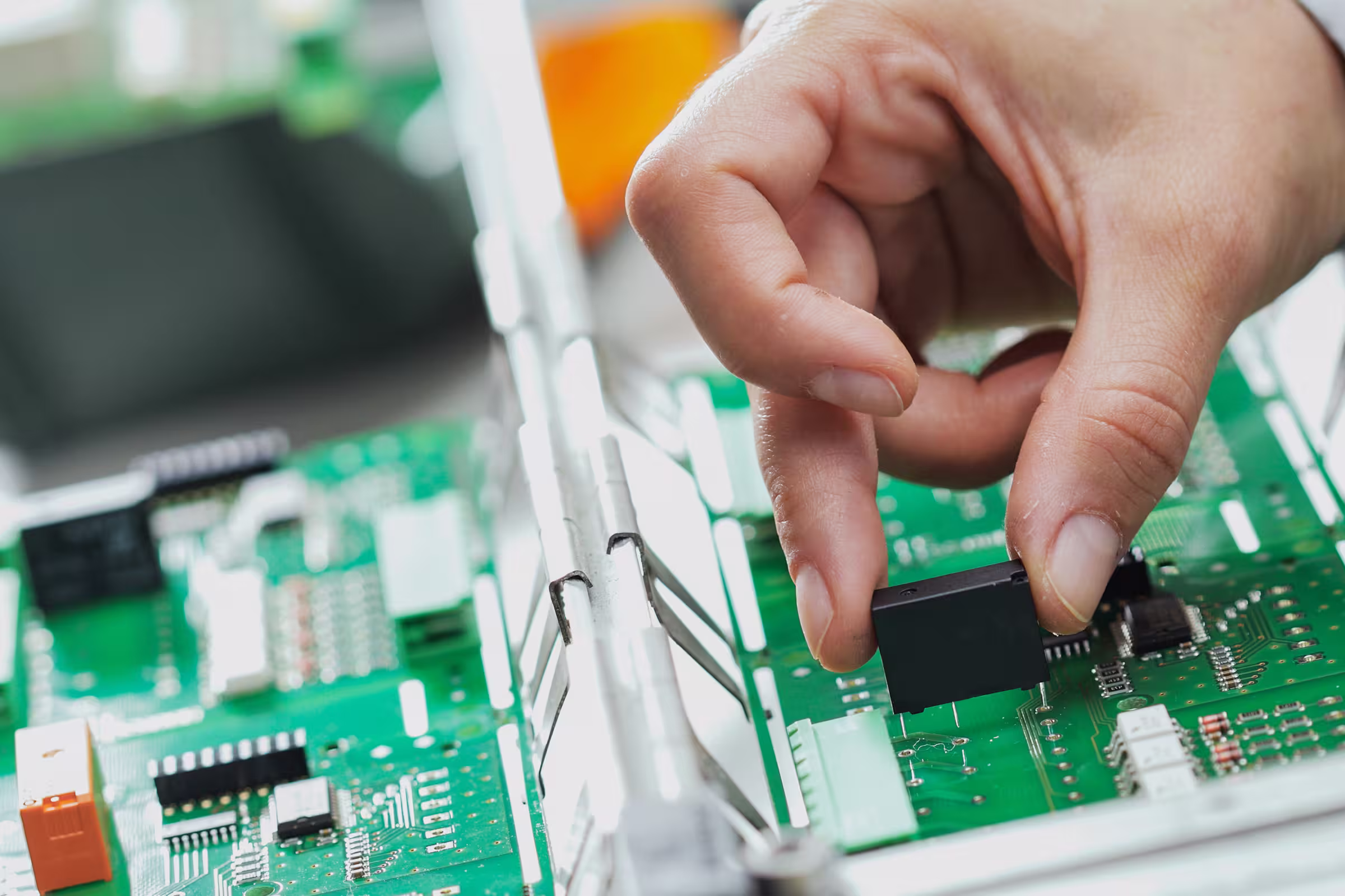 Hand setzt ein elektronisches Bauteil auf eine grüne Leiterplatte ein.