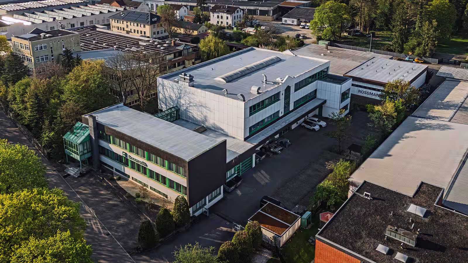 Luftaufnahme des modernen Firmengebäudes Rossmanith mit Parkplätzen und umgeben von Bäumen im Industriegebiet.